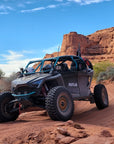 FastLab Polaris RZR with teal winch bumper and roll cage driving on a red rock trail in the desert