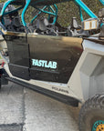 Polaris off-road vehicle with black FastLab rock slider steps and teal roll cage parked on pavement.